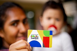 Imagem: divulgação Mulher segurando um cartão do bolsa família com bebê no colo