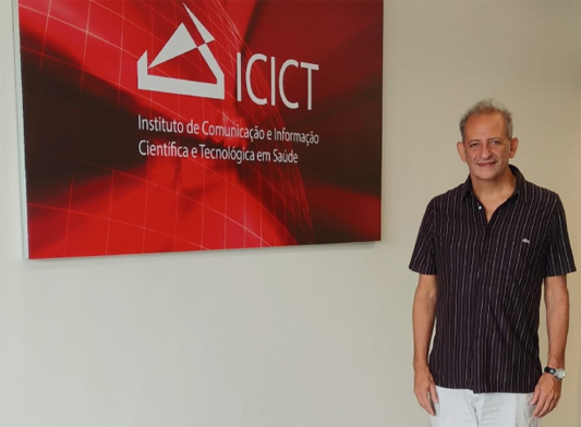 Mario Carlon de pé, em frente a um quadro escrito Icict