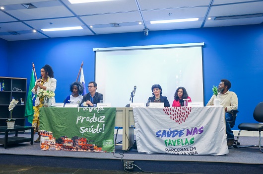 Foto de participantes à mesa do evento com bandeiras em exposição