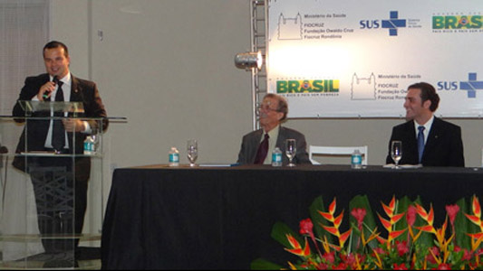 Ricardo discursa no púlpito, e os outros dois observam sentados à mesa