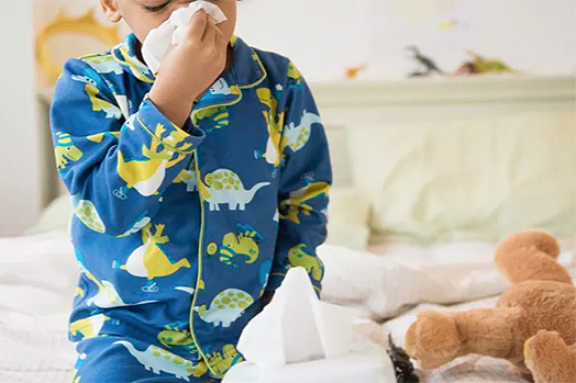 Foto de menino negro de pijama e assoando o nariz