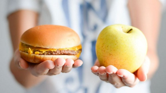 Uma maça em uma mão e um hamburger em outra