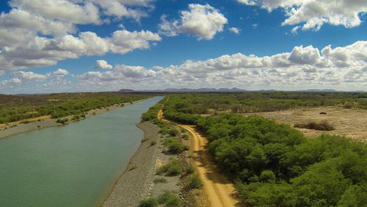 Rio corta paisagem de mata e céu azul com nuvens