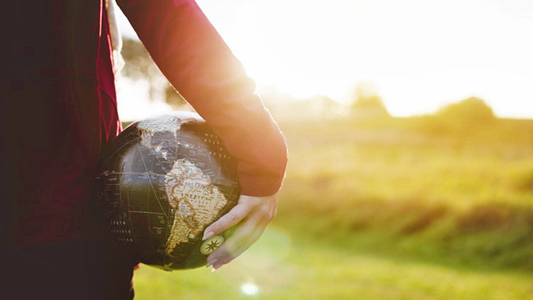 Mulher com um globo com o mapa do mundo em baixo do braço