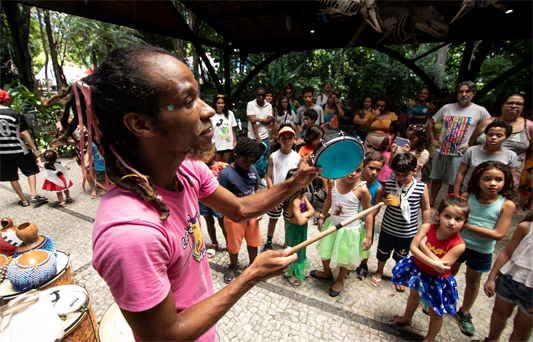 Animador tocando pandeiro para crianças no Campus da Fiocruz em Manguinhos