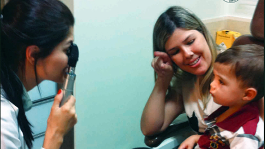 Foto de uma criança com a mãe sendo atendida pela oftalmologista
