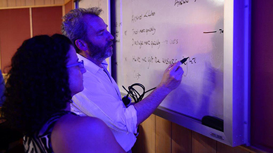 Professor escrevendo no quadro com aluna ao lado