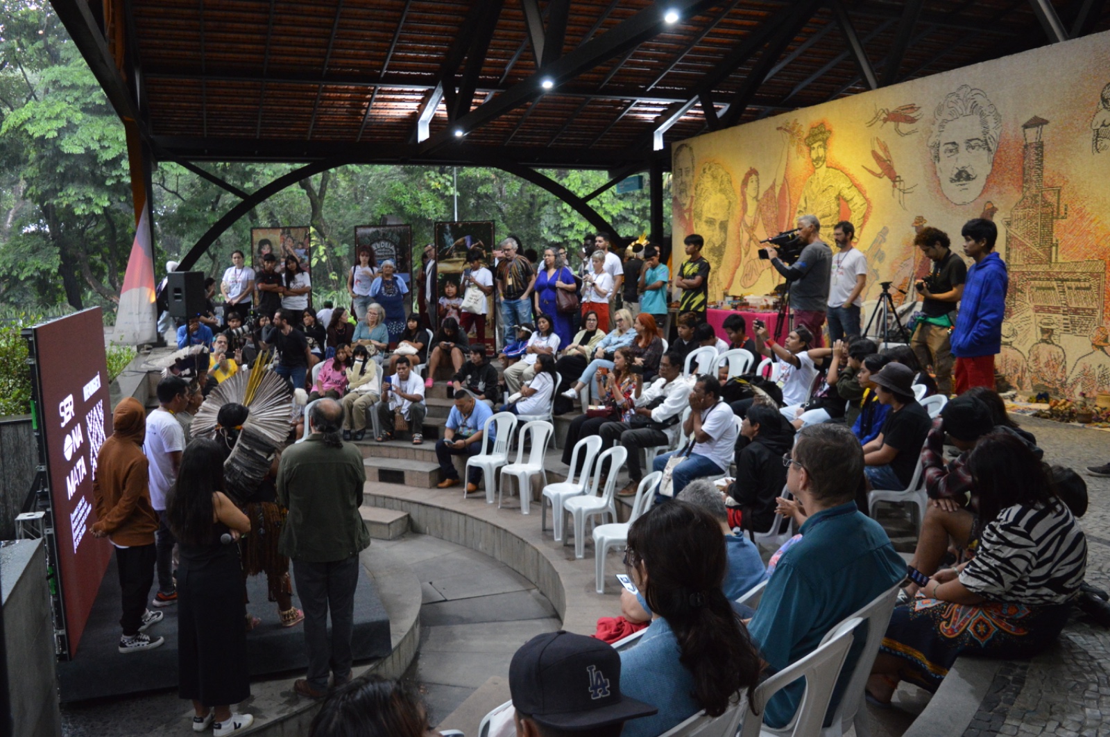 Auditório cheio durante mesa do evento “Abril Indígena” na Fiocruz, com painel de convidados e público atento.
