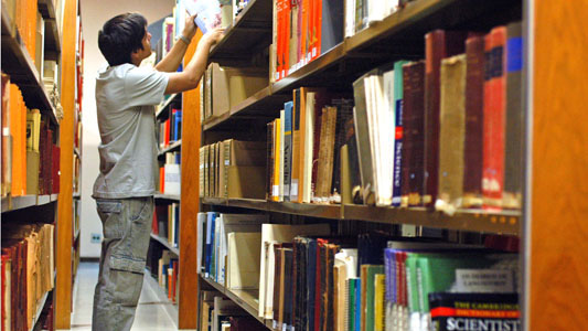Jovem procurando livro em estante de biblioteca