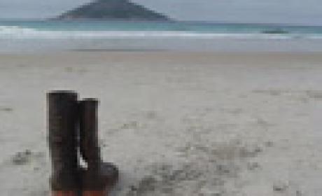 Paisagem de praia ao fundo e um par de botas