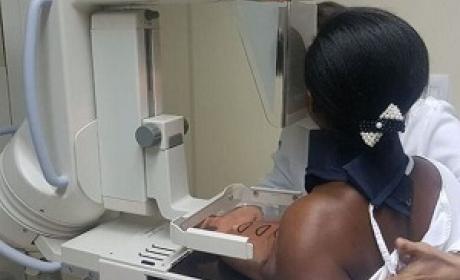Mulher de costas realizando exame de mamografia com auxílio de enfermeira