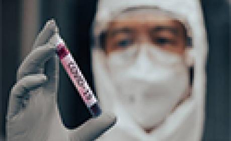 Técnico de laboratório em traje de EPI segurando amostra de sangue contendo Covid-19