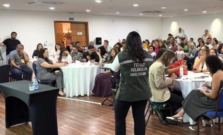 Imagem com uma sala lotada, ao centro uma mulher de cabelos castanhos longos palestrando aos demais