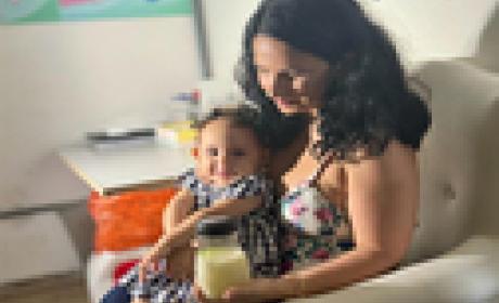 Mulher segura uma criança no colo e também um refratário cheio de leite 