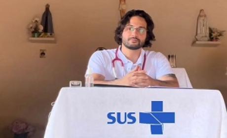 Médico sentado em uma mesa onde tem uma toalha de mesa com Logo do SUS