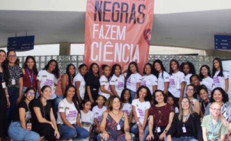 Meninas e Mulheres em Movimento para a Ciência Jovens meninas e mulheres em frente ao Aggeu Magalhães com laranja com os dizeres em branco "mulheres negras fazem ciência"