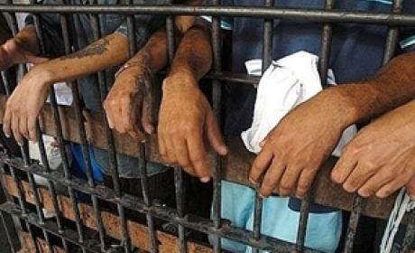 Mãos de pessoas presas apoiadas nas grades de um presídio